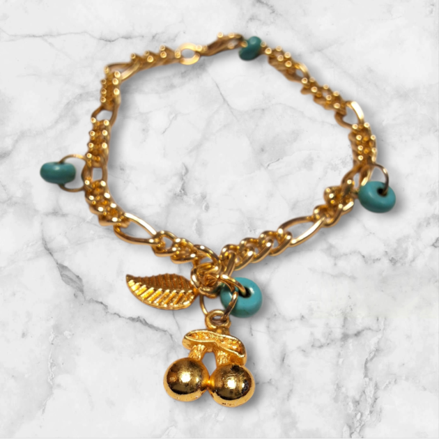 أسوارة ذهبية بقلادة كرز وورقة شجر وخرز فيروزي فوق خلفية رخامية بيضاء
