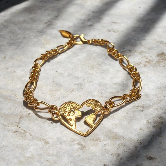 أسوارة ذهبية بقلادة قلب مفرغ لخريطة العالم فوق سطح رخامي