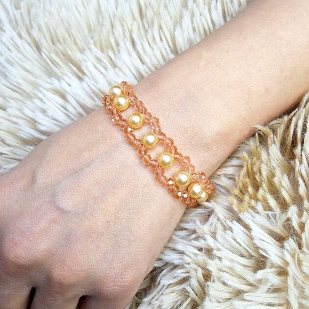أسوارة خرز عسلي ولؤلؤ ذهبي بتصميم حلقات مفرغة على معصم امرأة