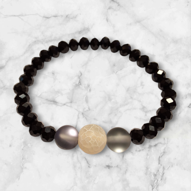 أسوارة خرز كريستال أسود وحجر طبيعي كريمي فوق خلفية رخامية بيضاء