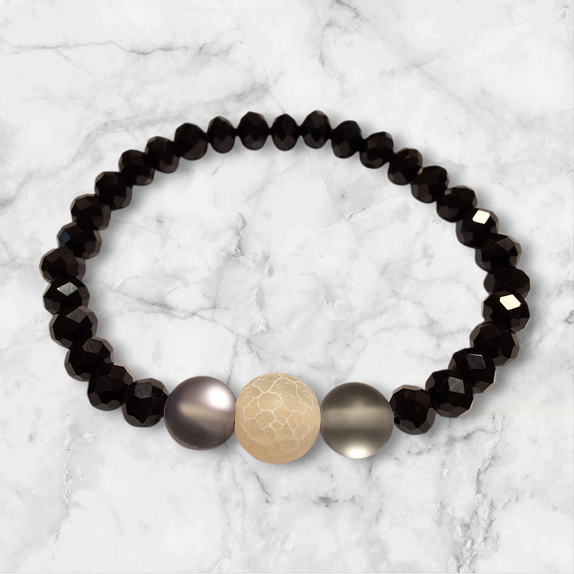 أسوارة خرز كريستال أسود وحجر طبيعي كريمي فوق خلفية رخامية بيضاء
