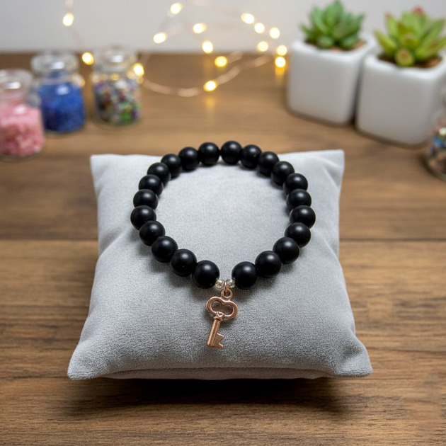 أسوارة خرز أسود مطفي بقلادة مفتاح ذهبية على وسادة رمادية