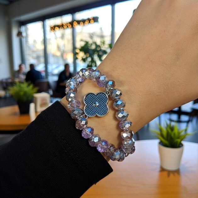 أسوارة كريستال أرجوانية بقلادة وردة زرقاء على معصم عارضة في مقهى هادئ