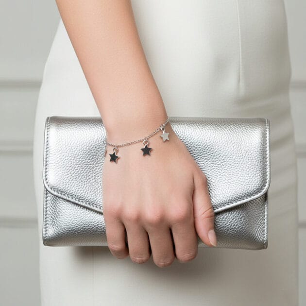 أسوارة فضية بقلادات نجوم متدلية على يد امرأة تمسك حقيبة فضية