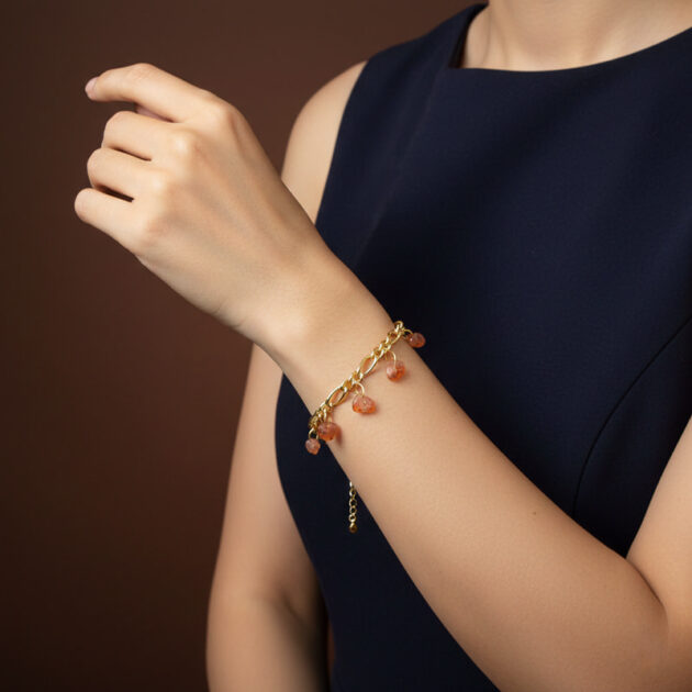 أسوارة ذهبية بقلادات أحجار عقيق برتقالية على معصم امرأة