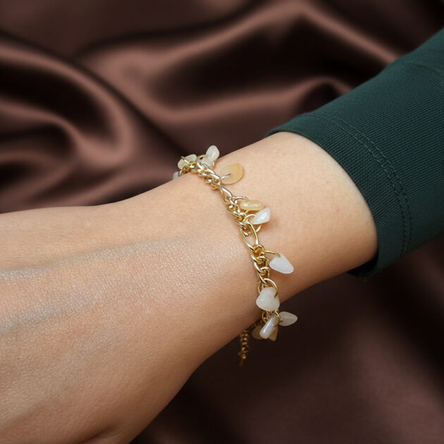 أسوارة ذهبية بقلادات أحجار قمر بيضاء على معصم امرأة