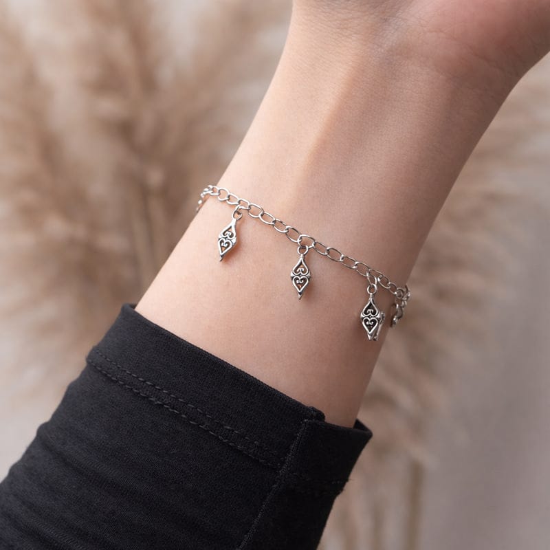 أسوارة فضية بقلادات معينة مزخرفة على معصم امرأة ترتدي أسود