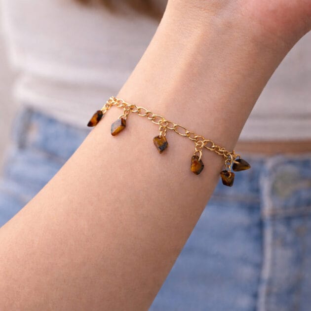 أسوارة ذهبية بقلادات أحجار عين النمر على معصم امرأة