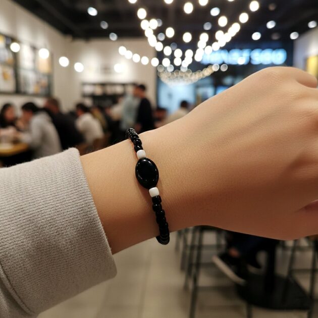 أسوارة خرز أسود ناعمة تتوسطها حبة بيضاوية تظهر على معصم يد عارضة في مقهى