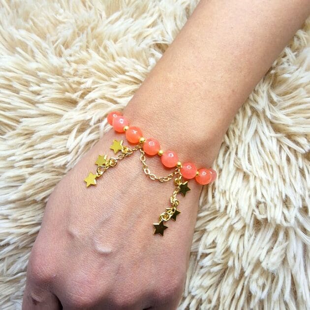 أسوارة خرز مرجاني برتقالي بقلادات نجوم ذهبية على معصم امرأة