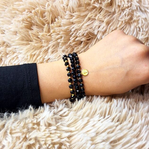 أسوارة خرز كريستال أسود بقلادة ذهبية دائرية على معصم امرأة