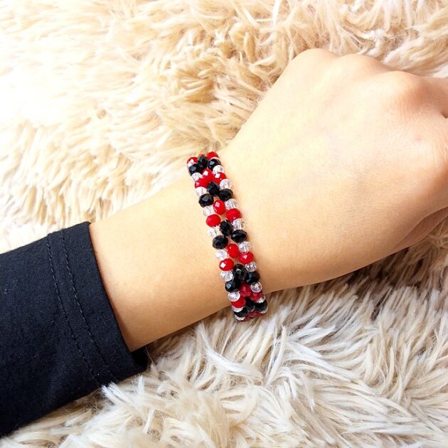 أسوارة عريضة من الكريستال الأسود والأحمر والشفاف على معصم امرأة