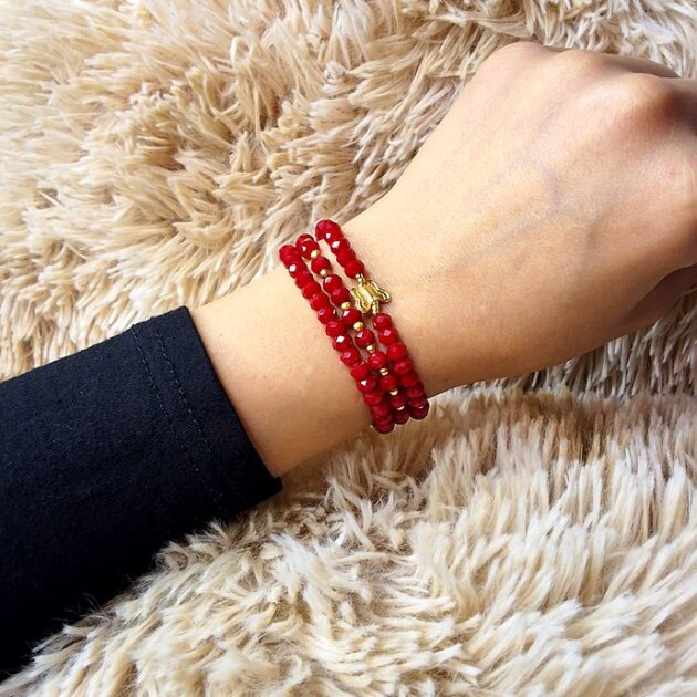 أسوارة خرز كريستال أحمر بقلادة فراشة ذهبية على معصم امرأة