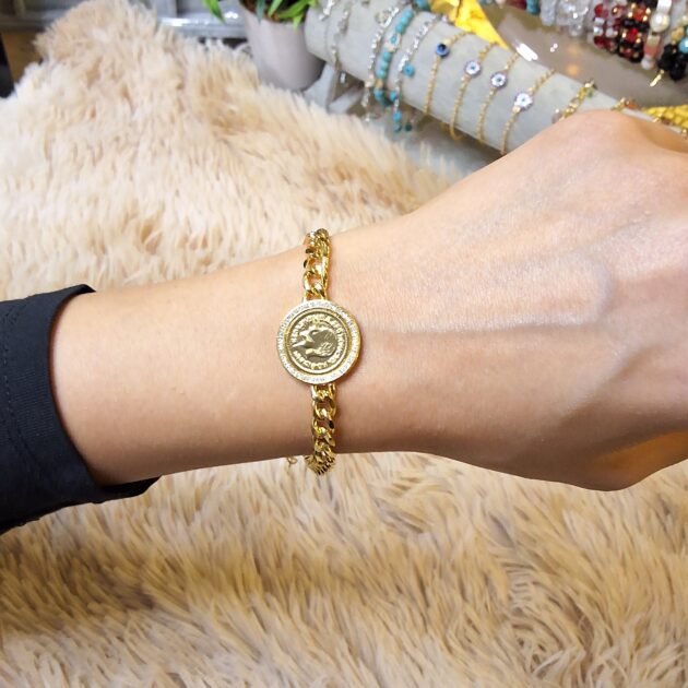 أسوارة ذهبية بنمط الجنزير مع ليرة مرصعة بالزركون تظهر على معصم يد عارضة من مجموعة متجر أميز شي.